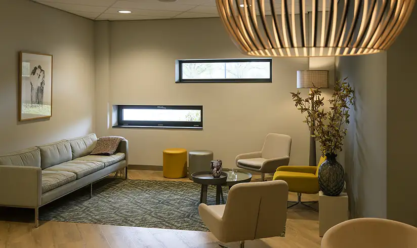 Een kamer met een grote zithoek met een grijze bank en verschillende kleuren fauteuils.